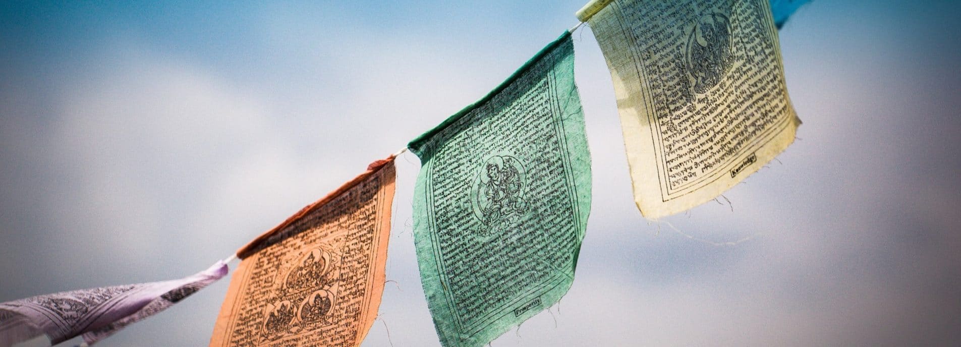 Bunte tibetische Gebetsfahnen wehen im Wind vor hellem Himmel. Die Stofffahnen zeigen traditionelle Mantras und Symbole in verschiedenen Farben.