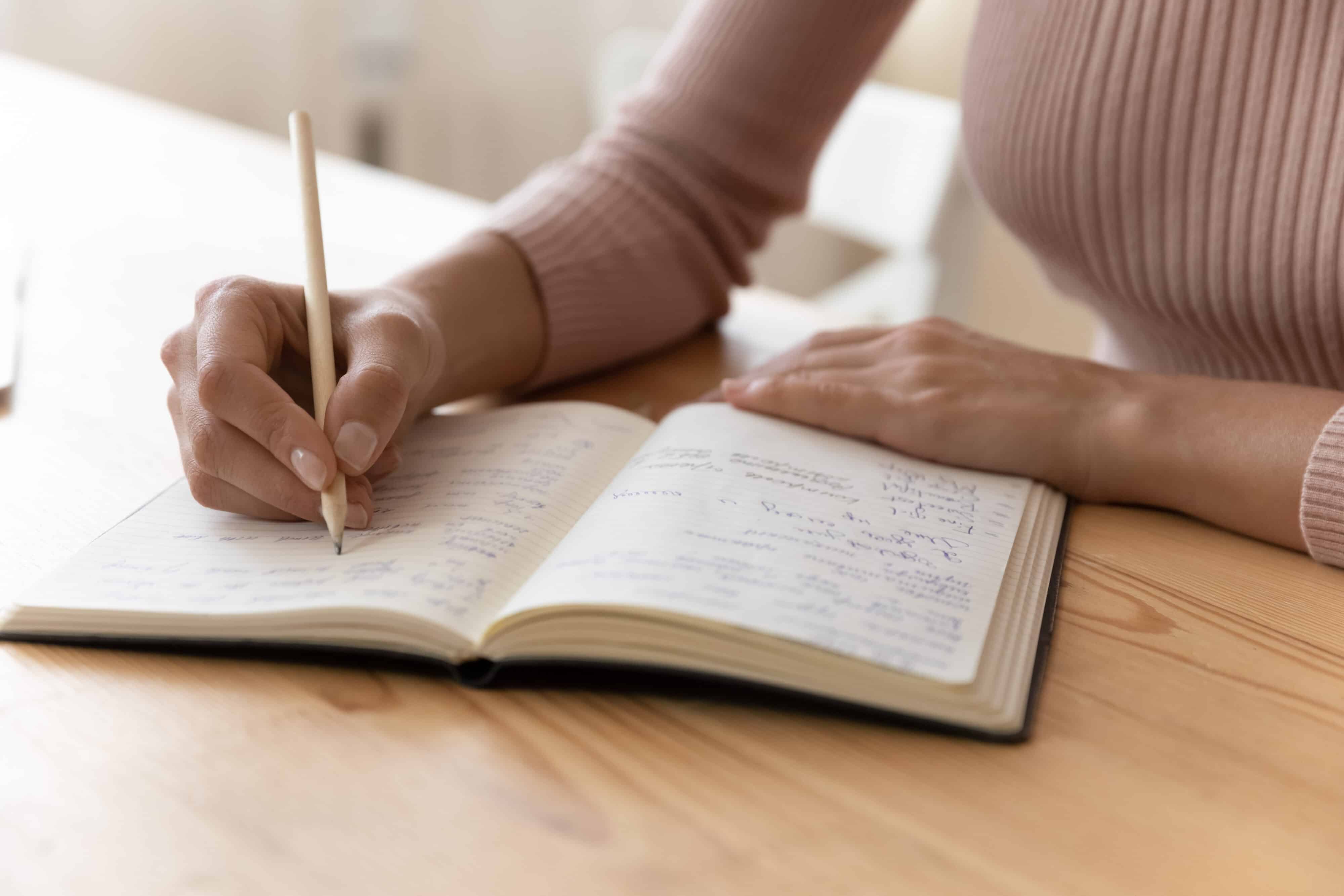 Auf dem Bild ist eine Hand zu sehen, die mit einem Stift auf Papier schreibt. Die Schrift auf dem Papier ist handgeschrieben, jedoch nicht vollständig lesbar. In der Bildmitte steht der Text „Click & Meet In the Heart of Being“.