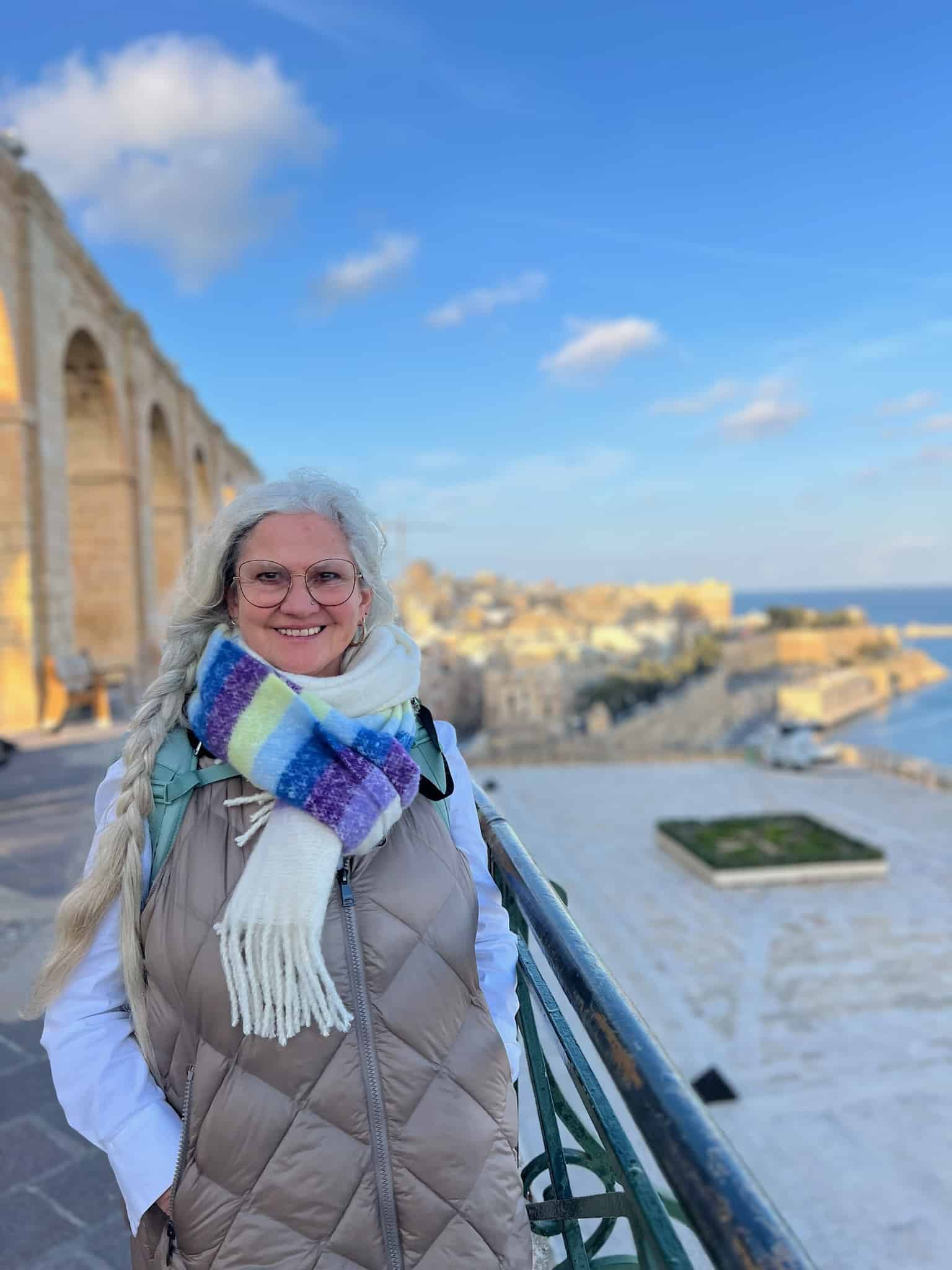 Das Bild zeigt Moti Theresia König mit einem weiß-blauen Schal an einem Aussichtspunkt in Valletta auf der Insel Malta.